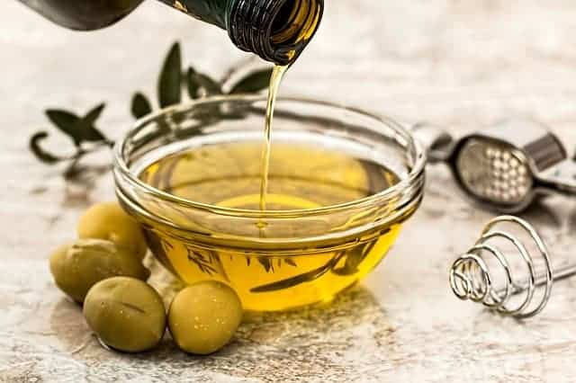 Öl in eine Schüssel gegossen, daneben grüne Oliven