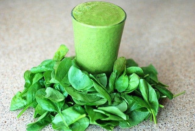 Ein Glas mit einem grünen Smoothie, rundherum Spinatblätter