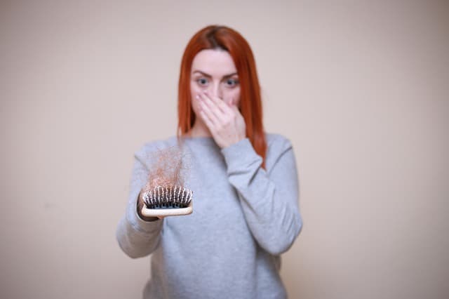 eine Frau schaut auf eine Haarbürste voller Haare