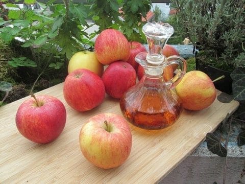 Frische Äpfel und eine Flasche Apfelessig auf dem Tisch