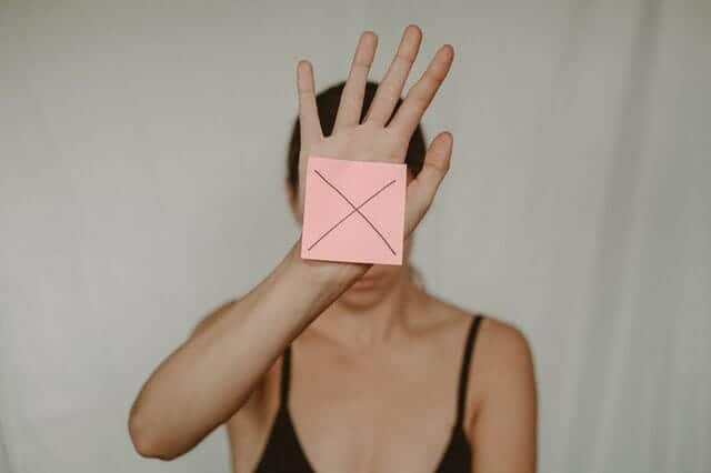  eine traurige Frau hält einen Pappkarton mit einem X vor sich