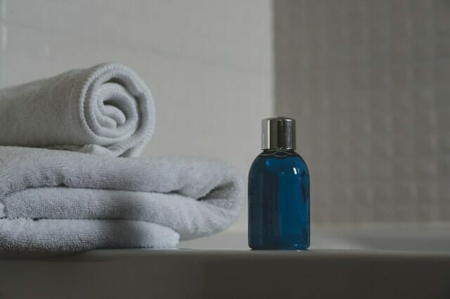  blaue Flasche mit Shampoo, daneben Handtücher