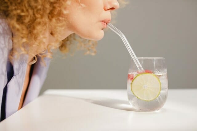  Frau trinkt Wasser durch einen Strohhalm