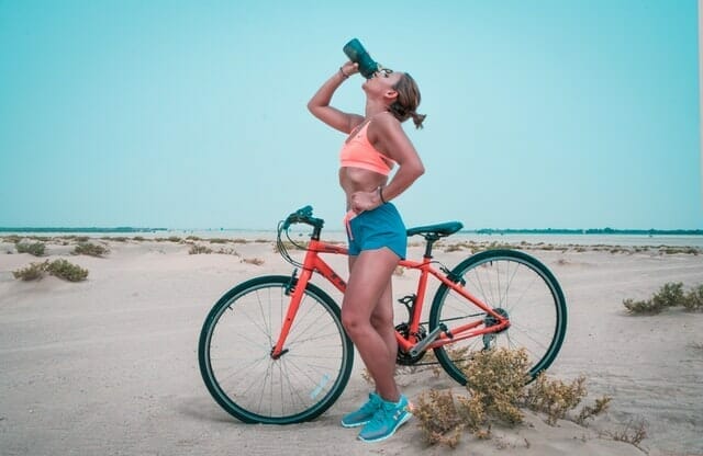  Frau trinkt nach einer Fahrradtour Wasser aus einer Flasche