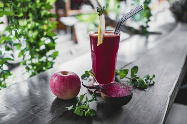  Rote-Bete-Saft in einem Glas, daneben ein Apfel und eine Rote Bete
