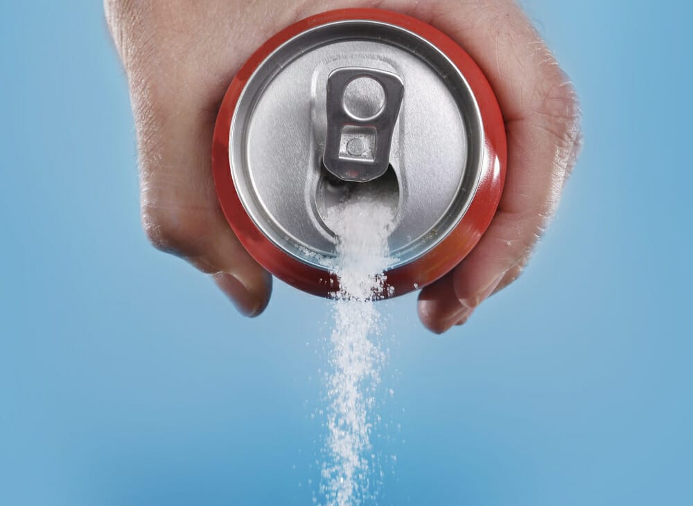  Weißer Zucker schwappt aus einer Coca-Cola-Dose