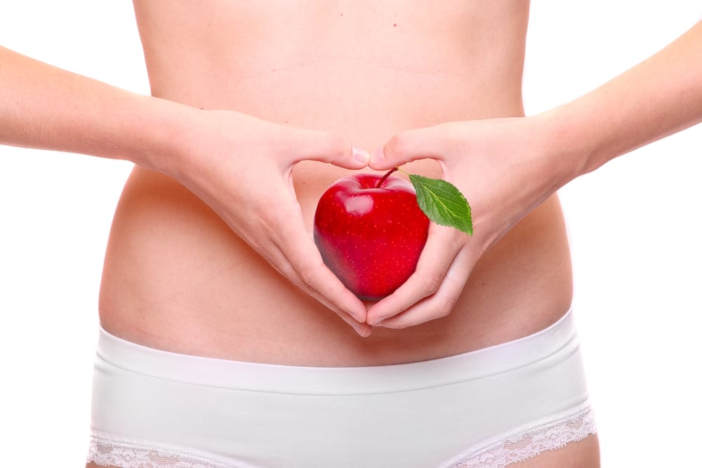  eine Frau hält einen Apfel an ihren Bauch